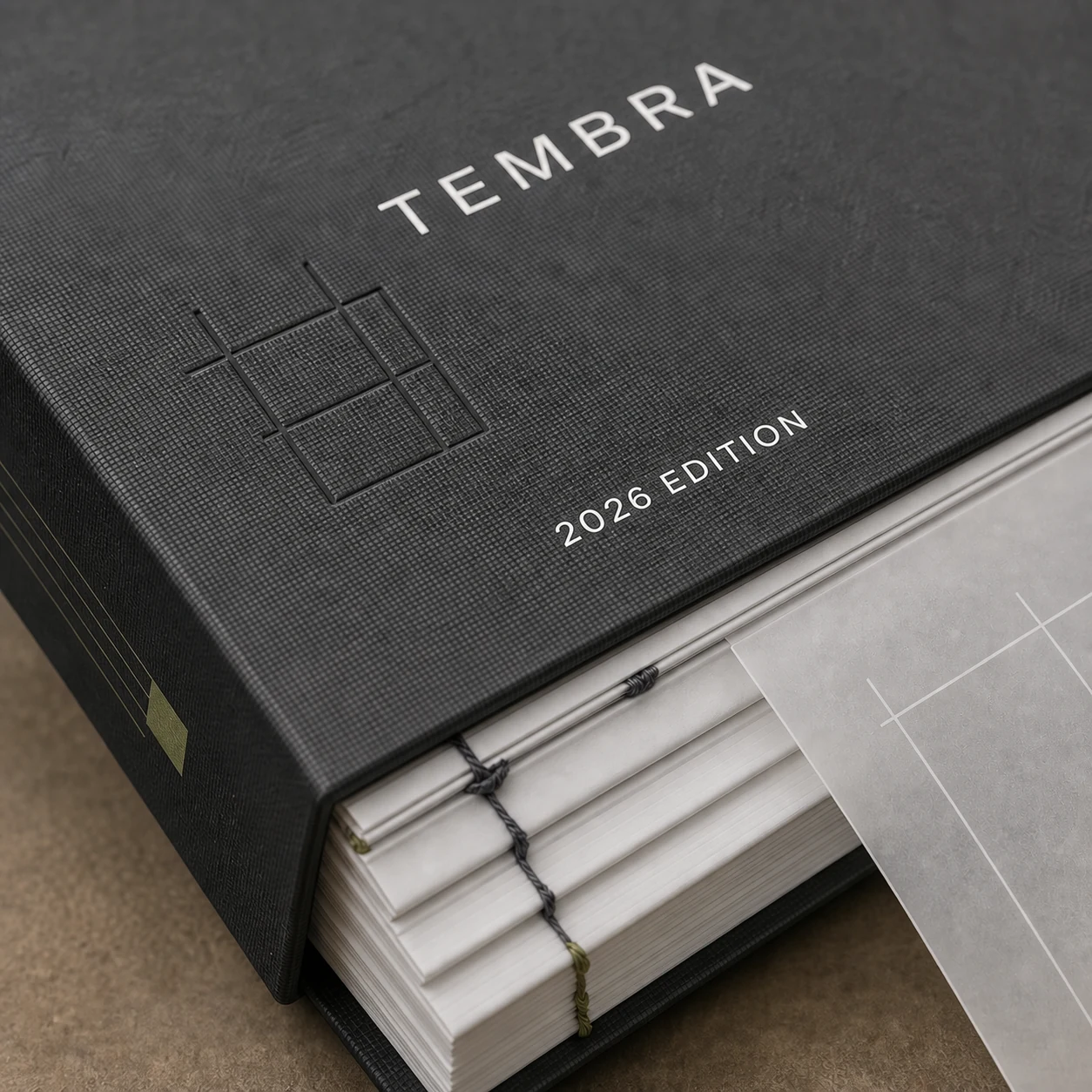 Macro detail of the TEMBRA catalog showing book cloth, blind debossing, printing, sewn signatures, thread and translucent page